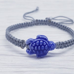 May include: A gray braided bracelet with a blue ceramic turtle charm.