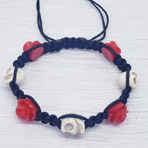 May include: Black cord bracelet with white skull and red rose beads.