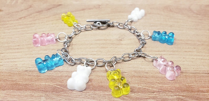 May include: A silver chain bracelet with seven gummy bear charms in various colors, including pink, blue, yellow, and white.