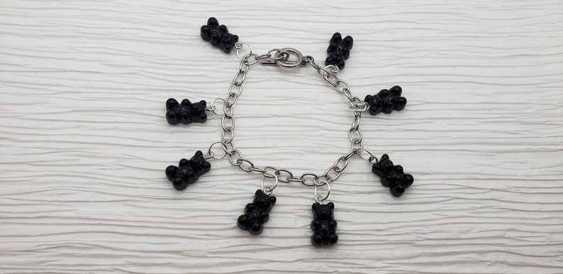 May include: A silver chain bracelet with black gummy bear charms. The bracelet has a lobster clasp closure.