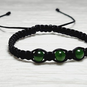 Puede incluir: Un brazalete trenzado negro con tres cuentas de jade verde.