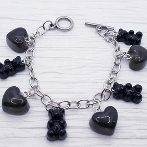 May include: A silver chain bracelet with black heart and gummy bear charms.