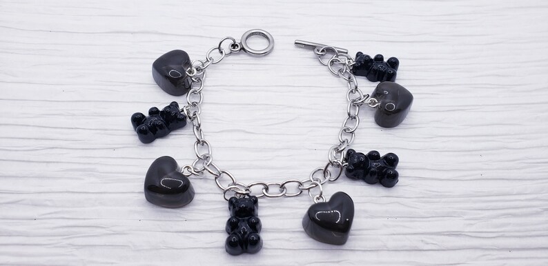 May include: A silver chain bracelet with black heart and gummy bear charms.