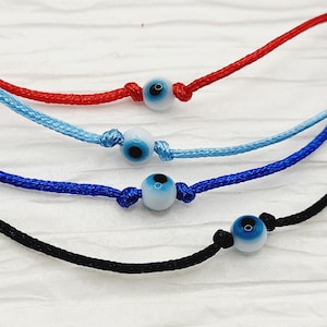 May include: Four different colored string bracelets with blue evil eye beads. The bracelets are red, light blue, dark blue, and black.
