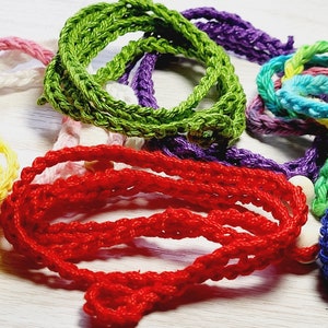May include: A collection of colorful, crocheted cords in various hues, including red, green, purple, and blue. The cords are arranged in a tangled, yet visually appealing, pattern. The texture of the yarn is clearly visible, suggesting a handmade craft item.