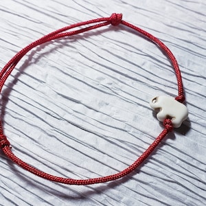May include: A red string bracelet with a white ceramic elephant charm.