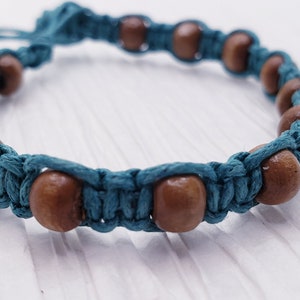 Puede incluir: Una pulsera de macram&eacute; turquesa con cuentas de madera. La pulsera presenta cuentas de madera marr&oacute;n espaciadas a lo largo del cord&oacute;n turquesa. El anudado de macram&eacute; crea un patr&oacute;n texturizado. La pulsera es ajustable.