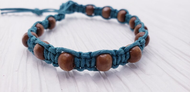 Puede incluir: Una pulsera de macram&eacute; turquesa con cuentas de madera. La pulsera presenta cuentas de madera marr&oacute;n espaciadas a lo largo del cord&oacute;n turquesa. El anudado de macram&eacute; crea un patr&oacute;n texturizado. La pulsera es ajustable.