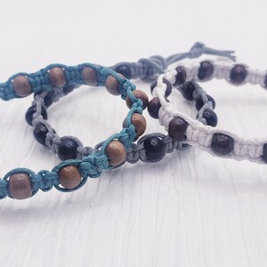 Puede incluir: Tres pulseras hechas a mano con cuentas de madera y cord&oacute;n anudado en verde azulado, gris y blanco. Las cuentas de madera son marrones y marr&oacute;n oscuro. Las pulseras son ajustables y tienen un dise&ntilde;o sencillo.