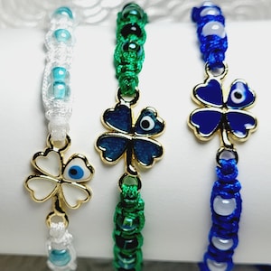 May include: Three macrame bracelets with gold-colored four-leaf clover charms. The bracelets are white, green, and blue, with matching beads. Each charm features an evil eye design, adding a touch of protection and style to the jewelry.