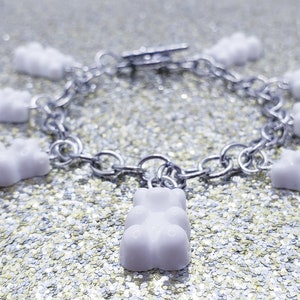 May include: A silver chain bracelet with white gummy bear charms. The bracelet is on a sparkly silver background.