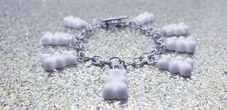 May include: A silver chain bracelet with white gummy bear charms. The bracelet is on a sparkly silver background.