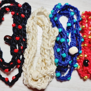 May include: Four strands of beaded necklaces in different colors and materials. One is black with red beads, one is white with clear beads, one is blue with turquoise beads, and one is red with gold beads.