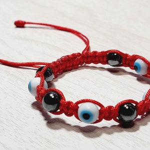 May include: Red macramé bracelet with alternating black and white beads, each with an eye design. The bracelet has an adjustable closure. This handmade bracelet is a fashion accessory.