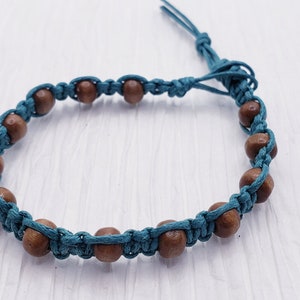 Puede incluir: Una pulsera de macram&eacute; turquesa con cuentas de madera. La pulsera est&aacute; hecha con cord&oacute;n turquesa, anudado para sujetar las cuentas de madera marr&oacute;n. La pulsera tiene un cierre ajustable de nudo corredizo.