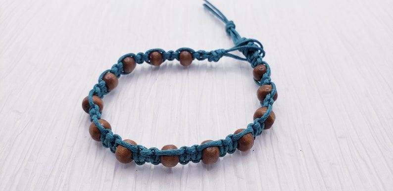 Puede incluir: Una pulsera de macram&eacute; turquesa con cuentas de madera. La pulsera est&aacute; hecha con cord&oacute;n turquesa, anudado para sujetar las cuentas de madera marr&oacute;n. La pulsera tiene un cierre ajustable de nudo corredizo.