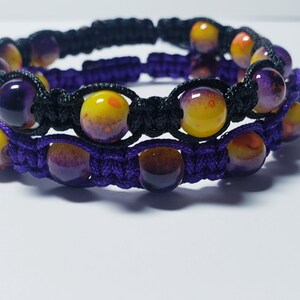 May include: A double-layered bracelet with purple and yellow beads, woven with black and purple cord.