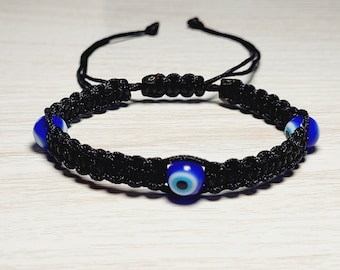 May include: Black braided bracelet with three blue evil eye beads. The bracelet has a sliding knot closure.