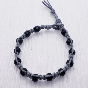Puede incluir: Un brazalete hecho a mano con cuentas negras ensartadas en un cord&oacute;n gris. El brazalete es ajustable con un cierre de nudo corredizo. Las cuentas est&aacute;n espaciadas uniformemente.