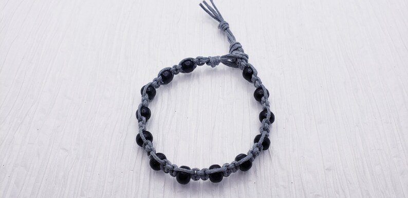 Puede incluir: Un brazalete hecho a mano con cuentas negras ensartadas en un cord&oacute;n gris. El brazalete es ajustable con un cierre de nudo corredizo. Las cuentas est&aacute;n espaciadas uniformemente.