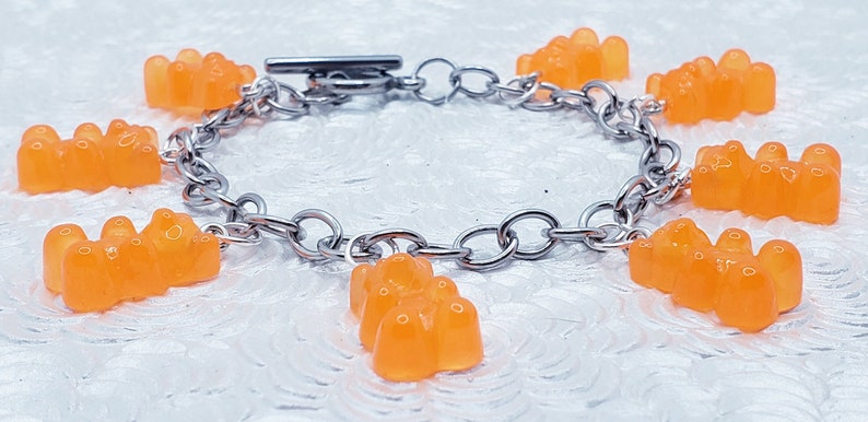 May include: A silver chain bracelet with orange gummy bear charms. The bracelet has a lobster clasp closure.