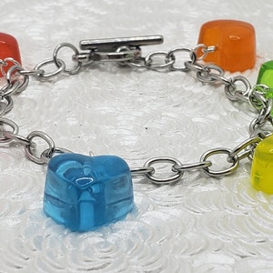 May include: A silver chain bracelet with five heart-shaped charms. The charms are made of clear plastic and are in the colors pink, orange, green, yellow, and blue.