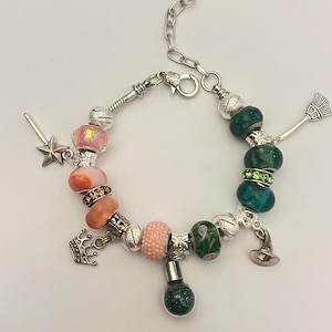 May include: A silver charm bracelet with various beads and charms. The bracelet features pink, orange, and green beads, along with charms like a star wand, crown, witch's hat, and a small bottle. The bracelet has a heart-shaped clasp.