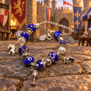 May include: A silver-tone charm bracelet featuring blue glass beads with white and red polka dots, evil eye patterns, and metallic charms including a rabbit, a goblet, a crown, a helmet, and a small tag with the text hand made.