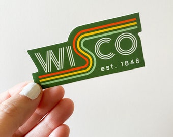 May include: A green sticker with the word "WISCO" in white, arched over a retro-style design with orange, yellow, and green stripes. The text "est. 1848" is below the word "WISCO".