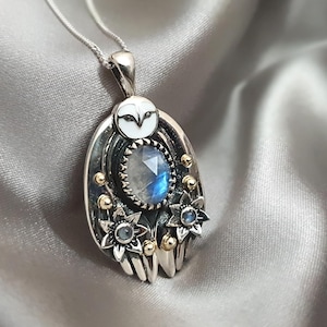 May include: A silver and gold pendant necklace featuring an owl with a moonstone gemstone and floral accents.