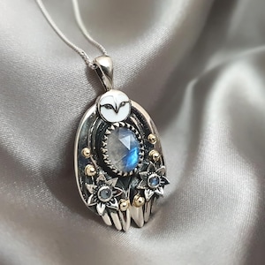 May include: Silver owl pendant necklace with a blue moonstone and gold accents. The owl has a white face and the moonstone is surrounded by a gold ring.