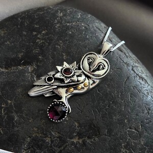 Puede incluir: Colgante de plata con forma de b&uacute;ho con un dise&ntilde;o detallado, con una flor y una piedra preciosa redonda de color rojo oscuro. Los ojos del b&uacute;ho est&aacute;n intrincadamente elaborados, y el colgante cuelga de una delicada cadena de plata. El colgante mide unos 5 cm de largo.