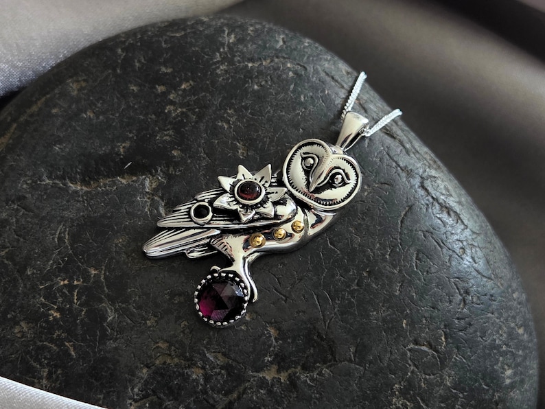 Puede incluir: Colgante de plata con forma de b&uacute;ho con un dise&ntilde;o detallado, con una flor y una piedra preciosa redonda de color rojo oscuro. Los ojos del b&uacute;ho est&aacute;n intrincadamente elaborados, y el colgante cuelga de una delicada cadena de plata. El colgante mide unos 5 cm de largo.
