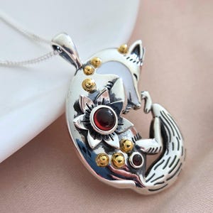 以下が含まれることがあります： 金色のアクセントと赤い宝石が特徴のシルバーフォックスのペンダント。ペンダントは、花と小さな赤い宝石を組み込んだ詳細なキツネのデザインが特徴です。シルバーチェーンに吊り下げられており、日常使いに最適です。