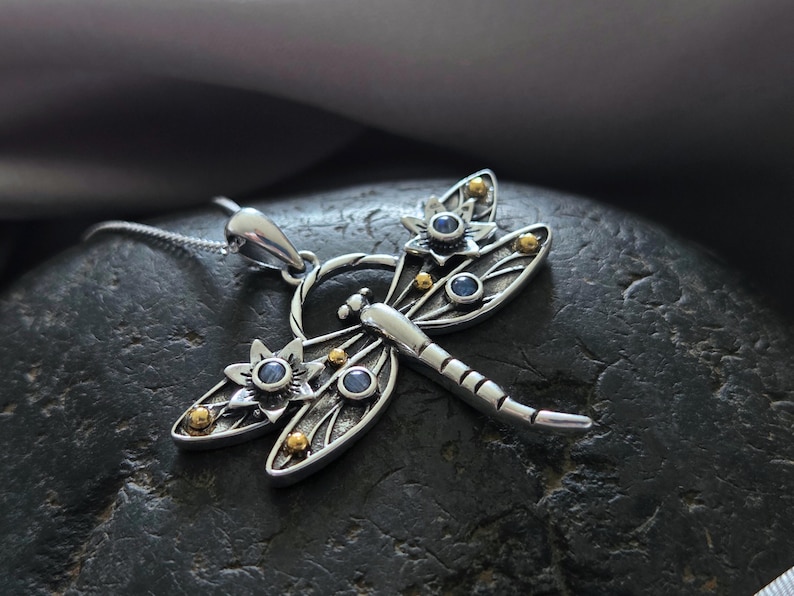 Pu&ograve; includere: Collana con ciondolo a forma di libellula in argento con dettagli blu e dorati. La libellula ha ali dettagliate e un corpo delicato.