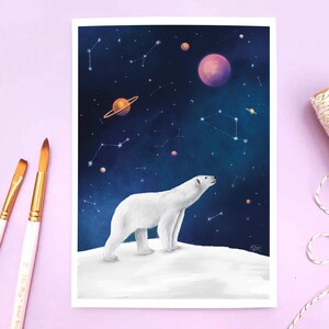 K&ouml;nnte beinhalten: Ein Kunstdruck mit einem wei&szlig;en Eisb&auml;ren auf einer schneebedeckten Oberfl&auml;che, der in einen Nachthimmel voller Planeten und Sternbilder blickt. Das Kunstwerk hat einen wei&szlig;en Rand. Zwei Pinsel und eine Rolle Schnur befinden sich an der Seite.