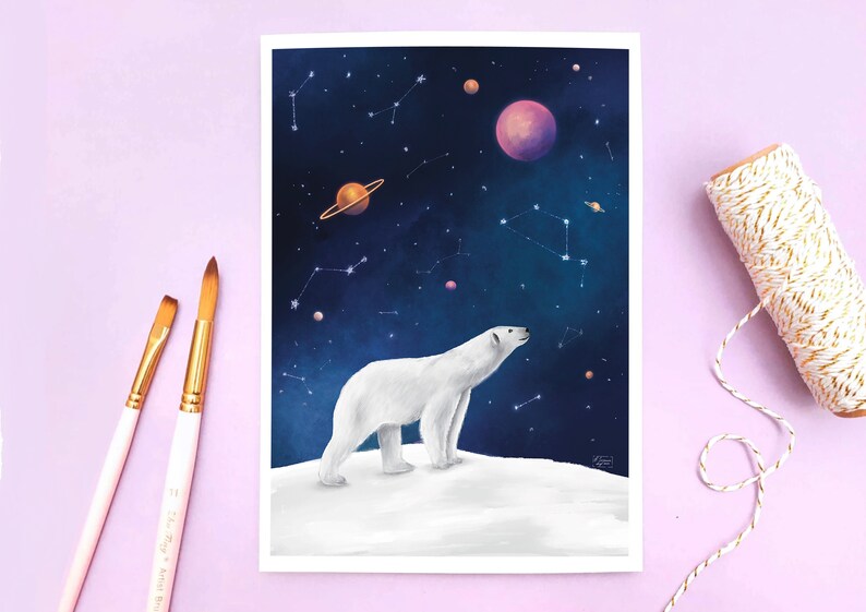 K&ouml;nnte beinhalten: Ein Kunstdruck mit einem wei&szlig;en Eisb&auml;ren auf einer schneebedeckten Oberfl&auml;che, der in einen Nachthimmel voller Planeten und Sternbilder blickt. Das Kunstwerk hat einen wei&szlig;en Rand. Zwei Pinsel und eine Rolle Schnur befinden sich an der Seite.