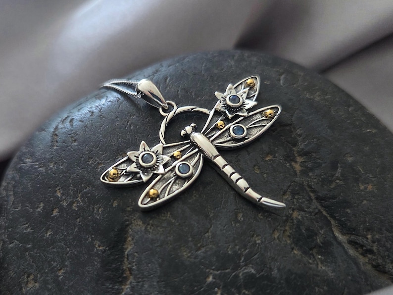 Pu&ograve; includere: Collana con ciondolo a forma di libellula in argento con dettagli blu e dorati. La libellula ha ali dettagliate e un corpo delicato.