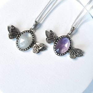 May include: Two silver necklaces with butterfly pendants. One pendant features a white gemstone, the other a purple gemstone.