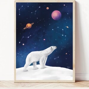 K&ouml;nnte beinhalten: Gerahmter Kunstdruck mit einem wei&szlig;en Eisb&auml;ren auf einer schneebedeckten Fl&auml;che, der in den Sternenhimmel blickt. Das Kunstwerk zeigt Planeten und Sternbilder in Lila, Orange und Blau.