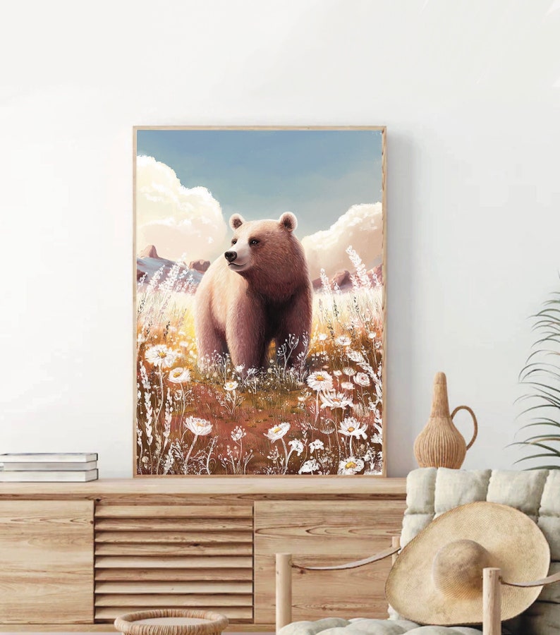 May include: A framed art print featuring a brown bear standing in a field of white wildflowers. The bear is the focal point, set against a backdrop of a blue sky with fluffy white clouds. The artwork has a warm, natural color palette.