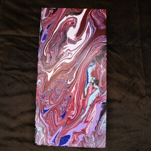 May include: An abstract canvas painting with a swirling, marbled effect. The artwork showcases a mix of colours, including red, white, blue, and purple, forming a dynamic and visually appealing composition. The rectangular canvas is set against a brown backdrop.