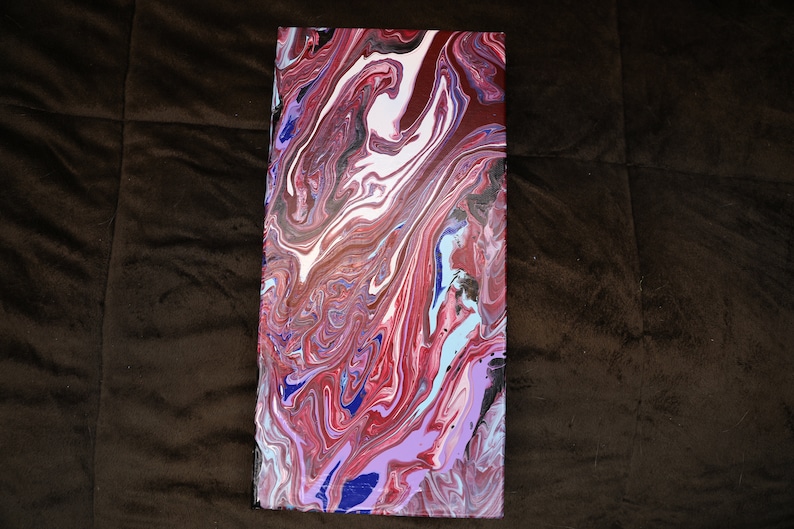 May include: An abstract canvas painting with a swirling, marbled effect. The artwork showcases a mix of colours, including red, white, blue, and purple, forming a dynamic and visually appealing composition. The rectangular canvas is set against a brown backdrop.