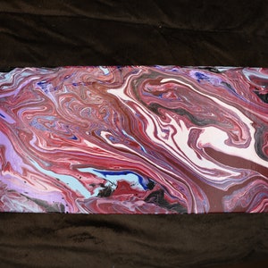 May include: Rectangular abstract painting with a fluid, marbled design. The artwork features a blend of colours, including shades of red, white, blue, and black, creating a dynamic and swirling pattern. The canvas is rectangular.