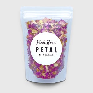 May include: A clear, resealable plastic pouch filled with dried pink and yellow rose petals. A circular white label on the front features the text Pink Rose PETAL rosa canina in black, bold, and script lettering centered on the bag.