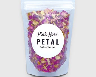 May include: A clear, resealable plastic pouch filled with dried pink and yellow rose petals. A circular white label on the front features the text Pink Rose PETAL rosa canina in black, bold, and script lettering centered on the bag.