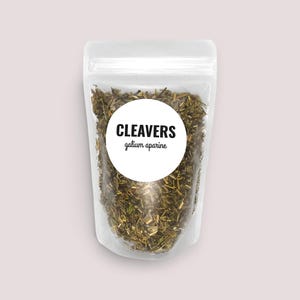 May include: A clear, resealable plastic pouch filled with dried, chopped green herbs. A circular white label on the front features the black text CLEAVERS and the smaller text galium aparine in a simple, clean, sans-serif and script font.