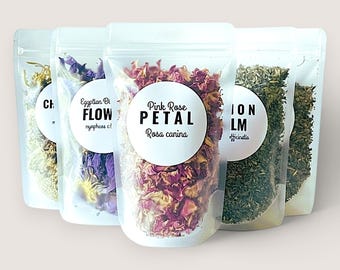 May include: Five clear stand-up pouches filled with dried botanicals. The center pouch features a white circular label with the text Pink Rose PETAL Rosa canina. Other pouches contain yellow, blue, and green dried herbs with visible labels.