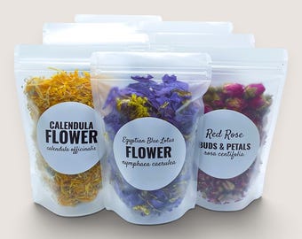 May include: Three clear stand-up pouches containing dried botanicals. The left pouch holds yellow calendula flowers, the center pouch contains blue Egyptian lotus flowers, and the right pouch holds red rose buds and petals, each with a white label.