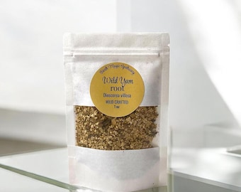May include: A clear, sealed bag filled with dried wild yam root. A gold circular label reads "Wild Yam root Dioscorea villosa WILD CRAFTED 1 oz" in black script. The bag is sitting on a glass surface.